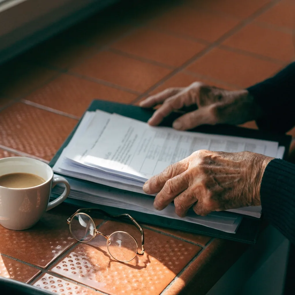 Manos de una mujer mayor con la carpeta de documentación sobre la mesa de su cocina